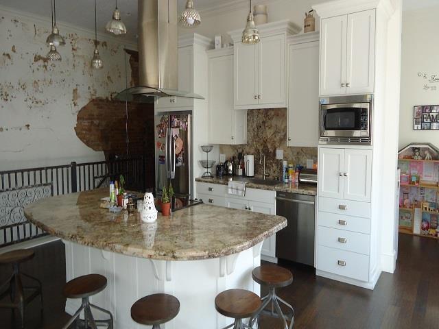 kitchen with pendant lighting, a kitchen island with sink, white cabinets, stainless steel appliances, and extractor fan