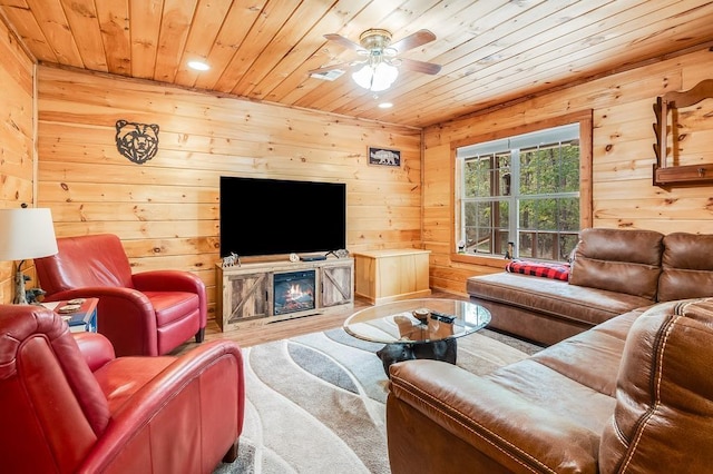 living room featuring wood walls, a glass covered fireplace, wooden ceiling, and ceiling fan