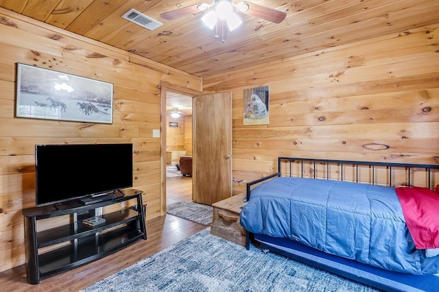bedroom with visible vents, wood finished floors, ceiling fan, wooden walls, and wooden ceiling