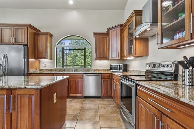 kitchen featuring sink, wall chimney range hood, light stone counters, a kitchen island, and appliances with stainless steel finishes