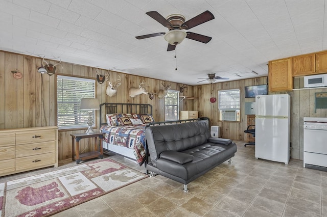 bedroom featuring ceiling fan, wooden walls, cooling unit, and white refrigerator