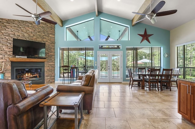 living room with french doors, ceiling fan, beam ceiling, high vaulted ceiling, and a stone fireplace