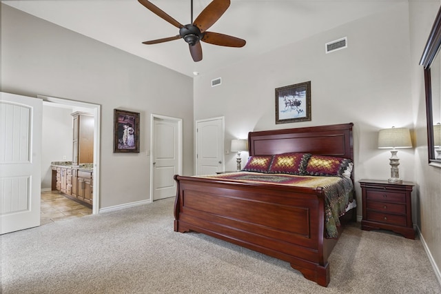 bedroom featuring ceiling fan, ensuite bathroom, a towering ceiling, and light colored carpet