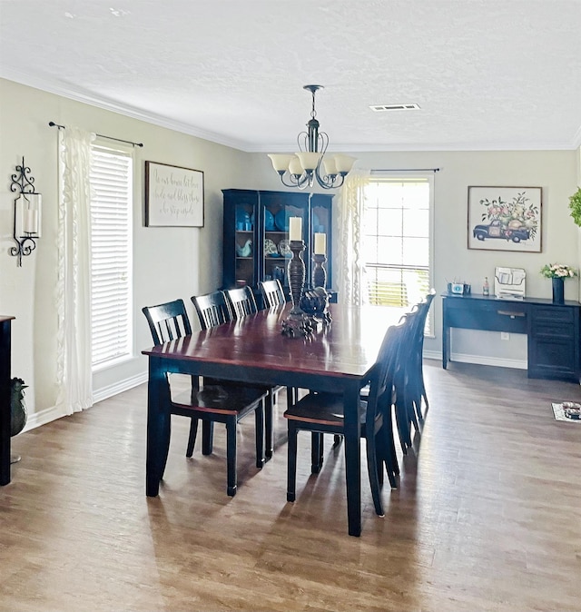 dining space featuring crown molding, wood-type flooring, a textured ceiling, and an inviting chandelier