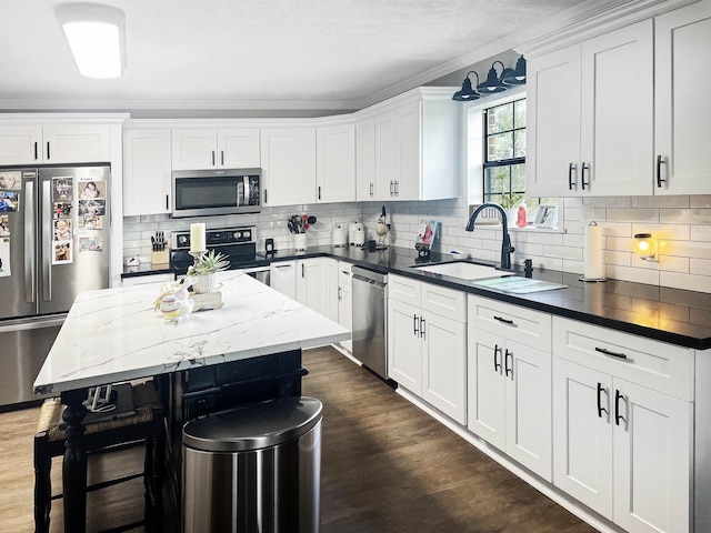 kitchen with appliances with stainless steel finishes, white cabinetry, a kitchen island, and sink