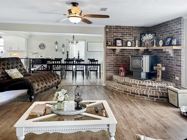 living room with ornamental molding, a textured ceiling, ceiling fan, hardwood / wood-style floors, and a wood stove