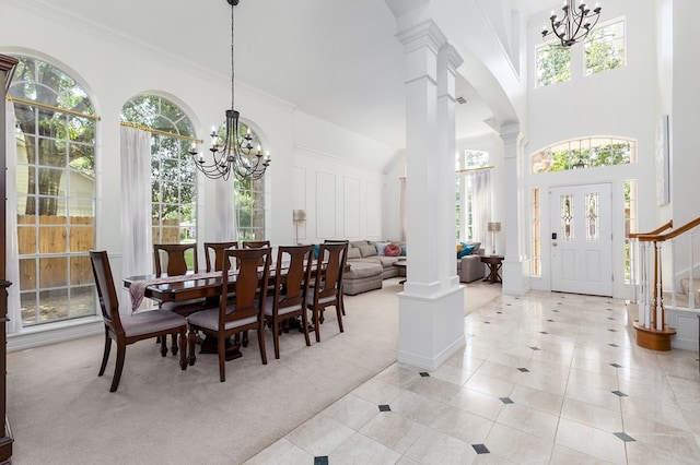 carpeted dining space with a chandelier, a towering ceiling, decorative columns, and a wealth of natural light