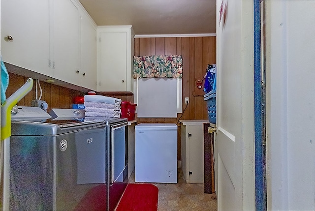 clothes washing area with washing machine and dryer, wooden walls, and cabinets