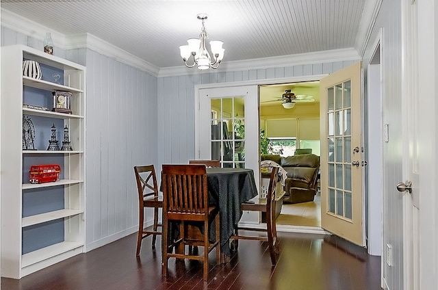 dining room with built in shelves, dark hardwood / wood-style floors, wood walls, ceiling fan with notable chandelier, and ornamental molding