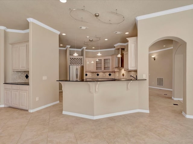 kitchen featuring arched walkways, stainless steel fridge, dark countertops, visible vents, and ornamental molding