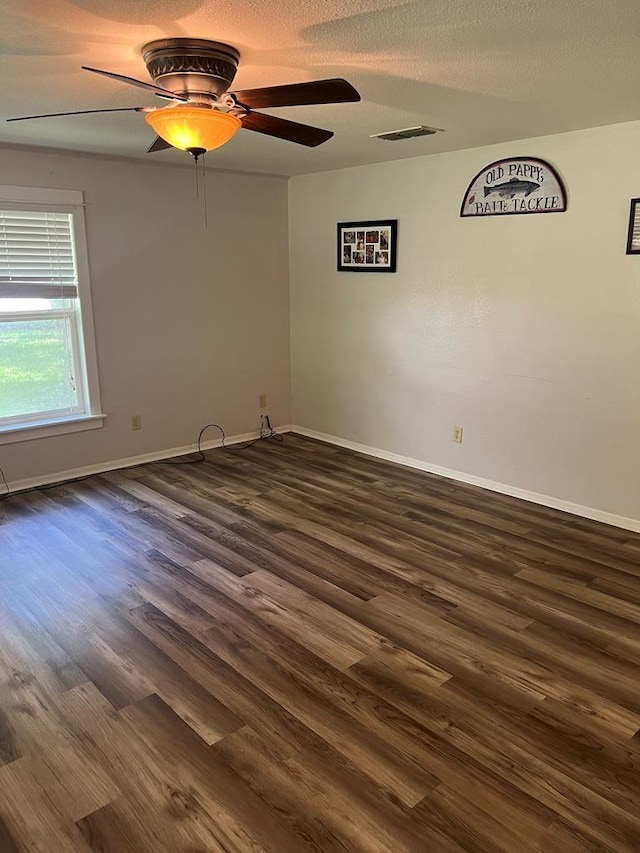 spare room featuring dark wood-style floors, visible vents, ceiling fan, a textured ceiling, and baseboards