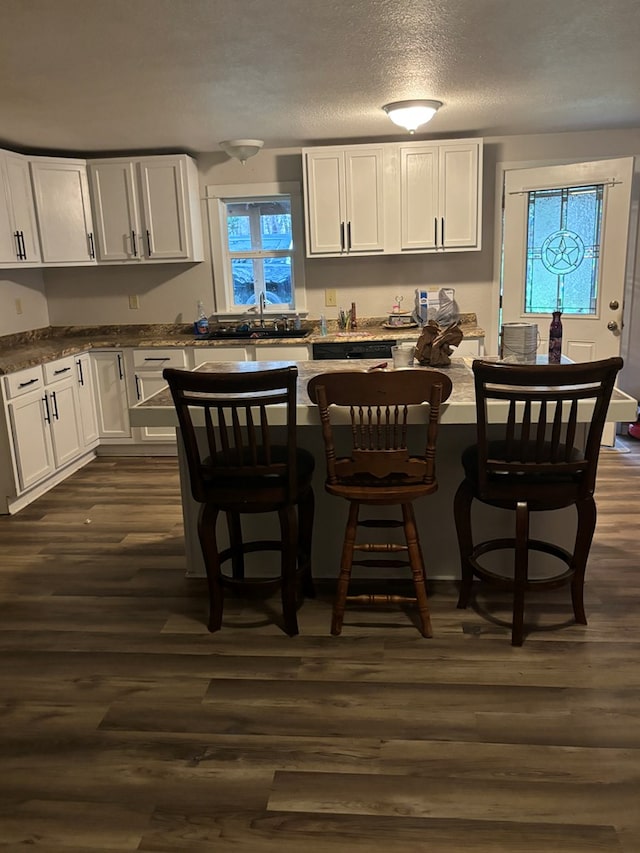 kitchen featuring white cabinets, a kitchen breakfast bar, sink, dark hardwood / wood-style floors, and light stone counters