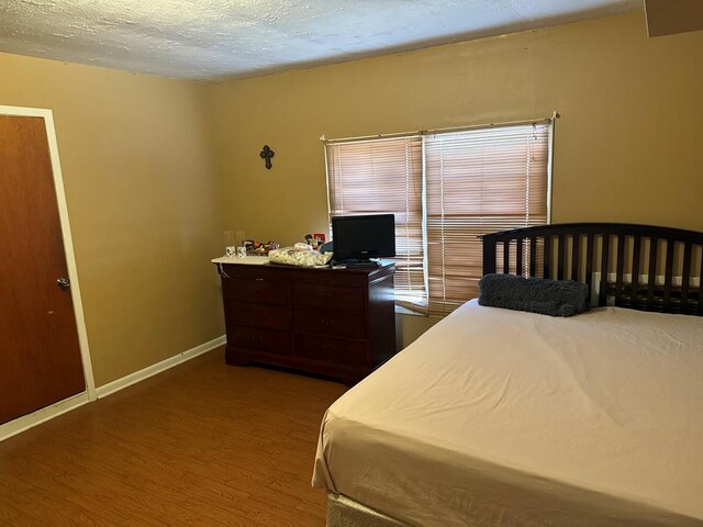 bedroom featuring a textured ceiling, wood finished floors, and baseboards