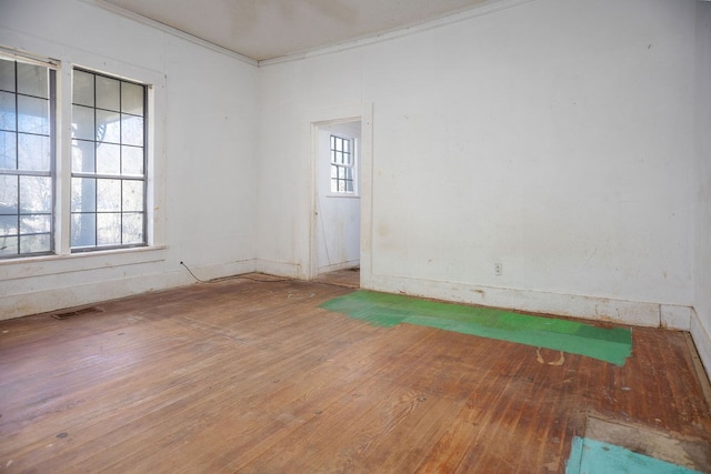 empty room with visible vents, ornamental molding, wood-type flooring, and a wealth of natural light