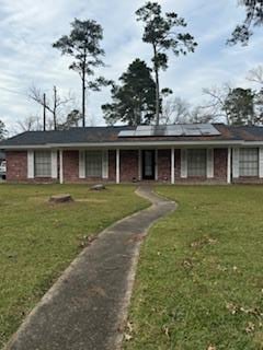 ranch-style home with roof mounted solar panels and a front yard