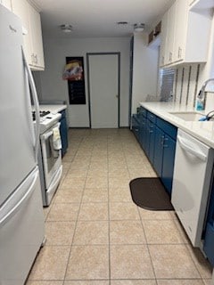 kitchen with light countertops, blue cabinets, a sink, light tile patterned floors, and white appliances