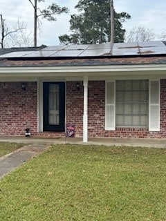 property entrance with a lawn, covered porch, and brick siding