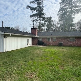 rear view of property featuring a chimney, central AC unit, and a yard