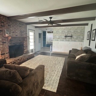 living area featuring beamed ceiling, a brick fireplace, and ceiling fan