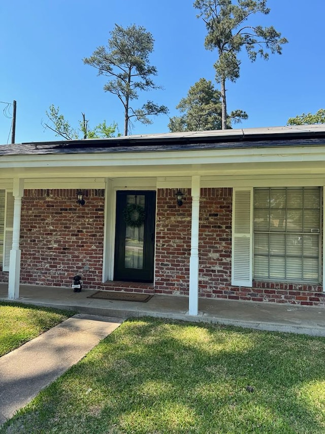 view of exterior entry with covered porch, a yard, and brick siding