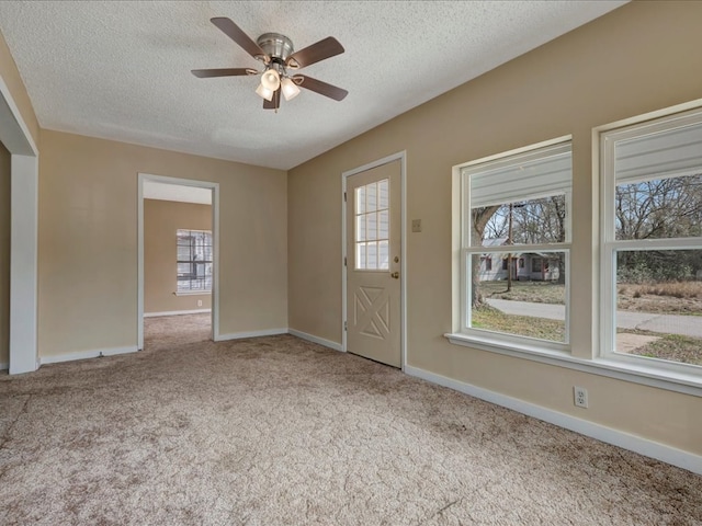 spare room with ceiling fan, a wealth of natural light, light colored carpet, and a textured ceiling