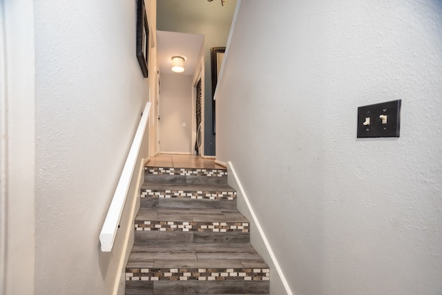 stairs featuring a textured wall, baseboards, and wood finished floors