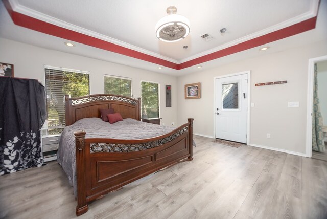 bedroom with a tray ceiling, light wood-style flooring, visible vents, and baseboards