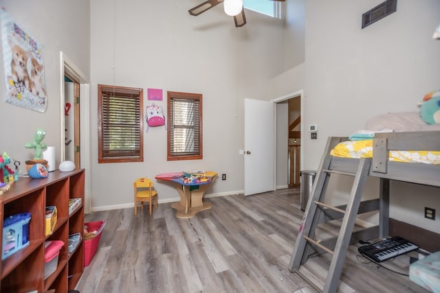 bedroom with light wood finished floors, baseboards, visible vents, a ceiling fan, and a towering ceiling