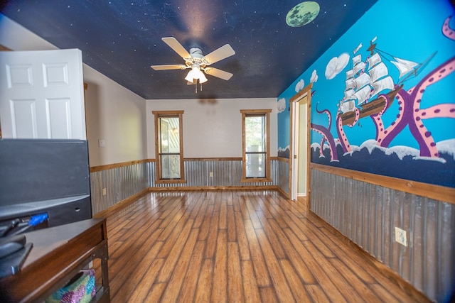 empty room featuring a ceiling fan, a wainscoted wall, and wood finished floors