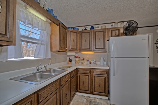 210 Cedar Rdg, Hemphill, TX 75948 - kitchen with a sink, a textured ceiling, freestanding refrigerator, brown cabinetry, and light countertops
