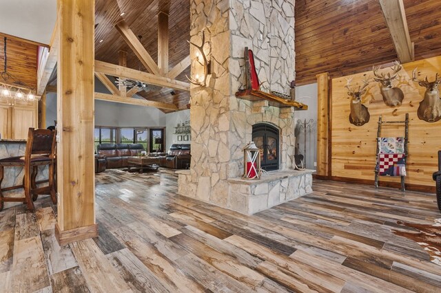 living room featuring wooden ceiling, a stone fireplace, high vaulted ceiling, hardwood / wood-style floors, and wooden walls