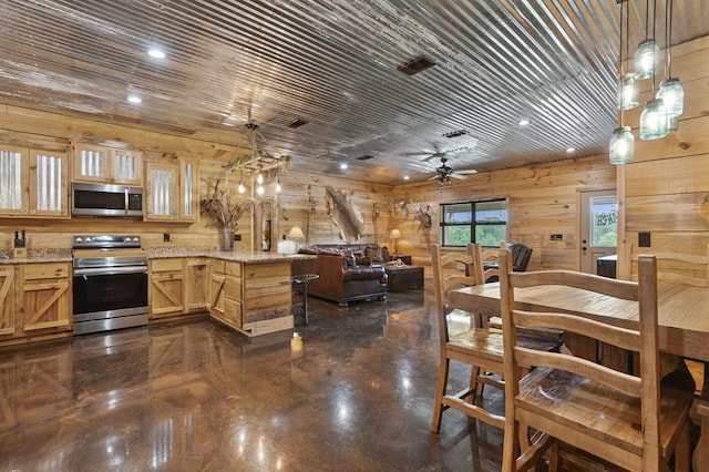 kitchen featuring light stone countertops, appliances with stainless steel finishes, ceiling fan, hanging light fixtures, and wood walls