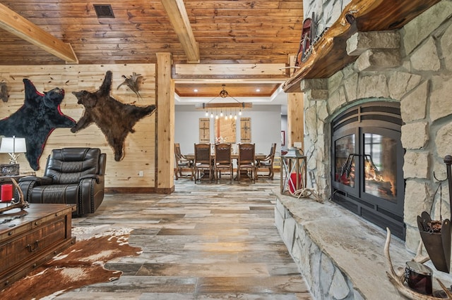 interior space with beam ceiling, a stone fireplace, light hardwood / wood-style flooring, and wood ceiling