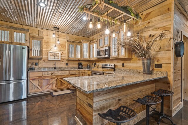 kitchen with kitchen peninsula, appliances with stainless steel finishes, light stone counters, hanging light fixtures, and wood walls