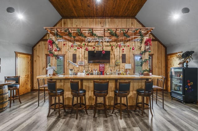 bar with wood walls, wooden ceiling, lofted ceiling, and hardwood / wood-style flooring