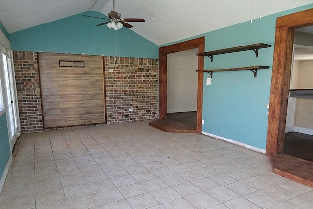 tiled empty room featuring ceiling fan, brick wall, and vaulted ceiling