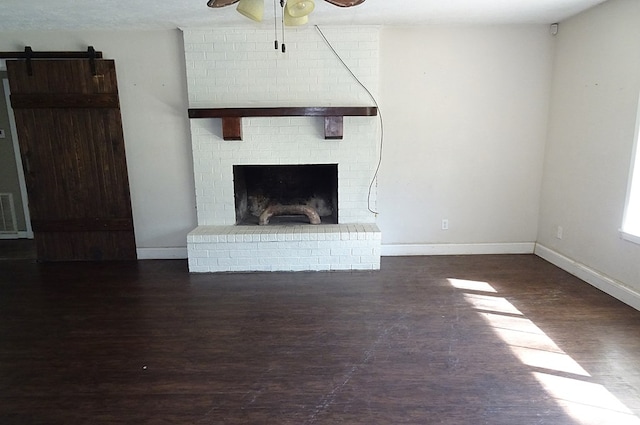 unfurnished living room featuring ceiling fan, dark hardwood / wood-style floors, a barn door, and a fireplace