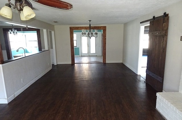 unfurnished dining area featuring french doors, a barn door, a textured ceiling, dark hardwood / wood-style flooring, and a chandelier