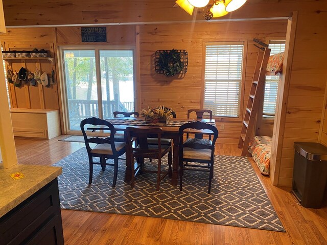 dining room with light wood-type flooring, plenty of natural light, and wood walls