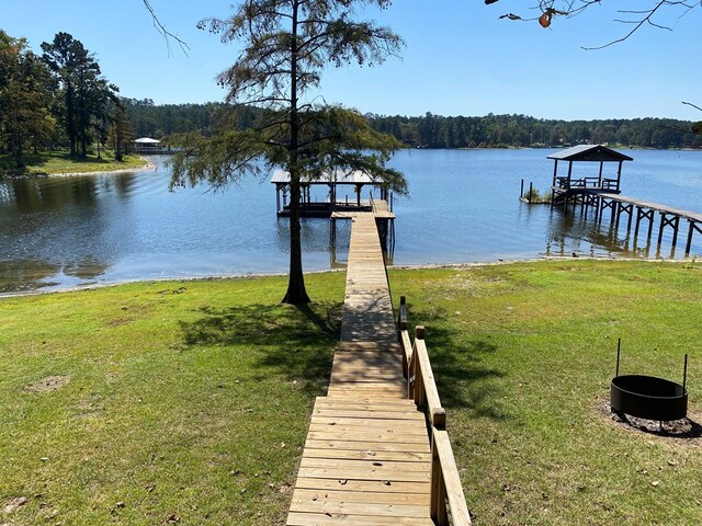 view of dock featuring a water view, an outdoor fire pit, and a lawn