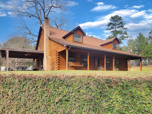 view of property exterior featuring a porch, an attached carport, a chimney, and log exterior