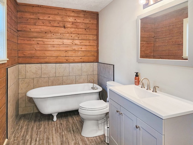 full bath with toilet, wood finished floors, a textured ceiling, vanity, and a freestanding tub