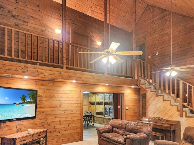 living area featuring a ceiling fan, wood walls, high vaulted ceiling, and stairs