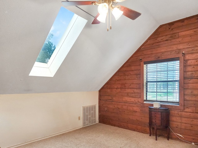 additional living space with carpet floors, lofted ceiling with skylight, wooden walls, and visible vents