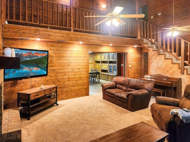 carpeted living area with ceiling fan, wooden walls, a high ceiling, and stairs