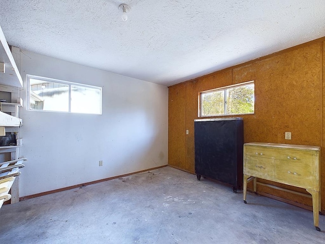 spare room with a textured ceiling, concrete floors, and wood walls