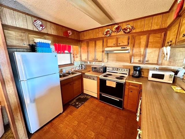 kitchen with parquet floors, white appliances, a textured ceiling, and wooden walls