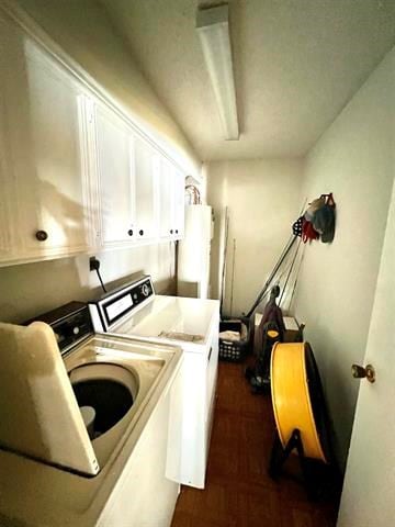 clothes washing area featuring water heater, washer and clothes dryer, dark parquet floors, and cabinets