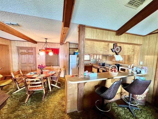 kitchen with hanging light fixtures, beamed ceiling, white refrigerator, wood walls, and a textured ceiling