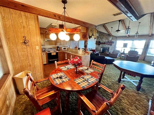 dining area featuring wood walls, vaulted ceiling with beams, ceiling fan, a fireplace, and a textured ceiling